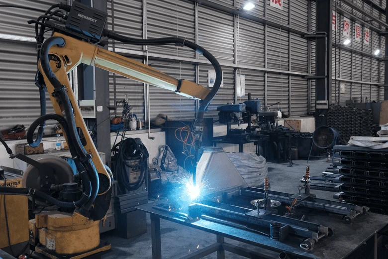 A robotic welding arm working on steel components in the HENER workshop