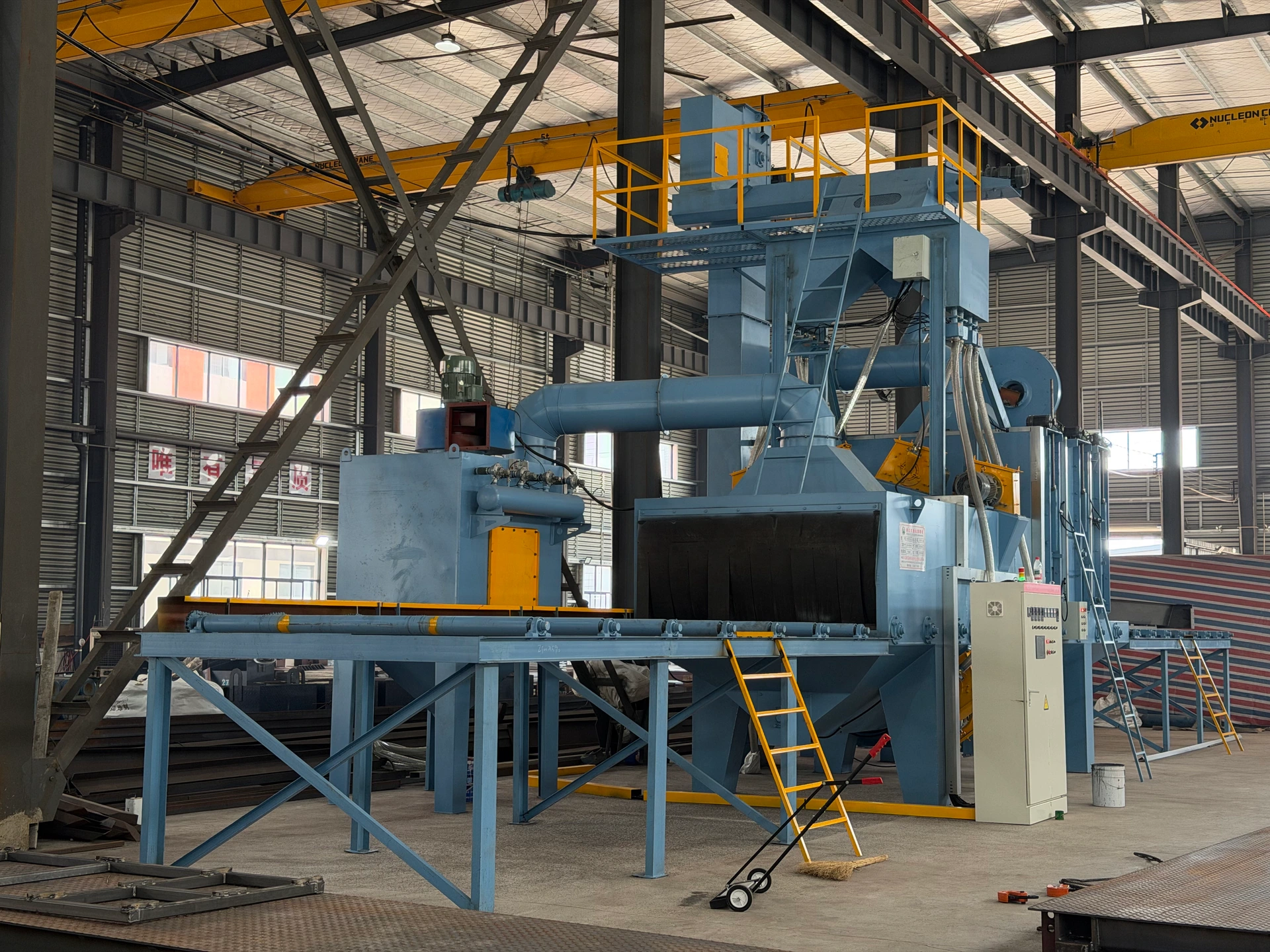 Shot-blasting equipment with a roller conveyor and access platform in the HENER workshop